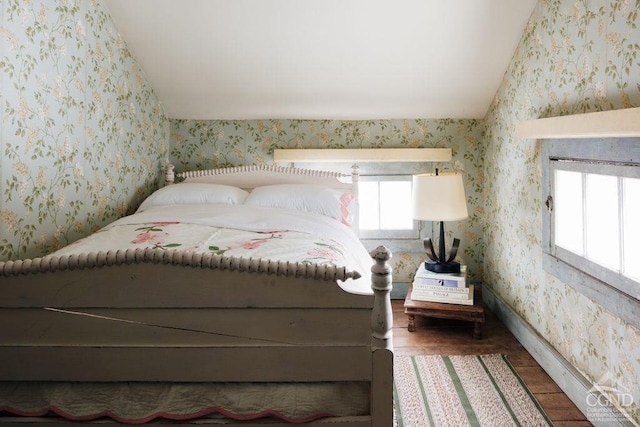 bedroom with wallpapered walls, multiple windows, vaulted ceiling, and wood finished floors