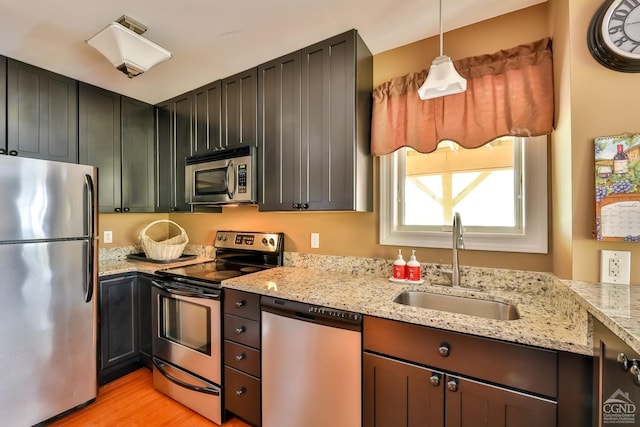 kitchen featuring pendant lighting, sink, light stone countertops, appliances with stainless steel finishes, and light hardwood / wood-style floors