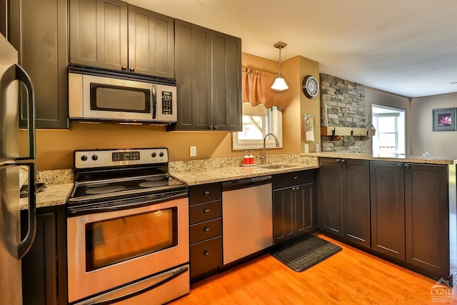 kitchen with sink, light hardwood / wood-style flooring, kitchen peninsula, decorative light fixtures, and appliances with stainless steel finishes