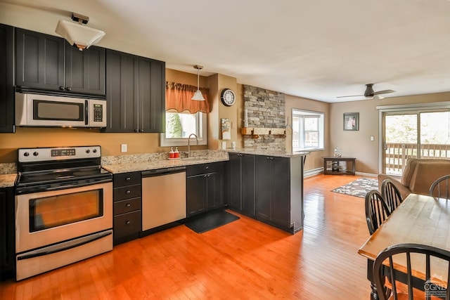 kitchen with kitchen peninsula, pendant lighting, stainless steel appliances, and a wealth of natural light