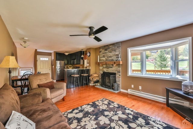 living room with a stone fireplace, ceiling fan, hardwood / wood-style floors, and a baseboard radiator