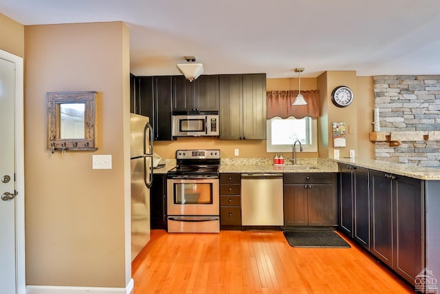 kitchen featuring light stone countertops, kitchen peninsula, light hardwood / wood-style floors, decorative light fixtures, and appliances with stainless steel finishes