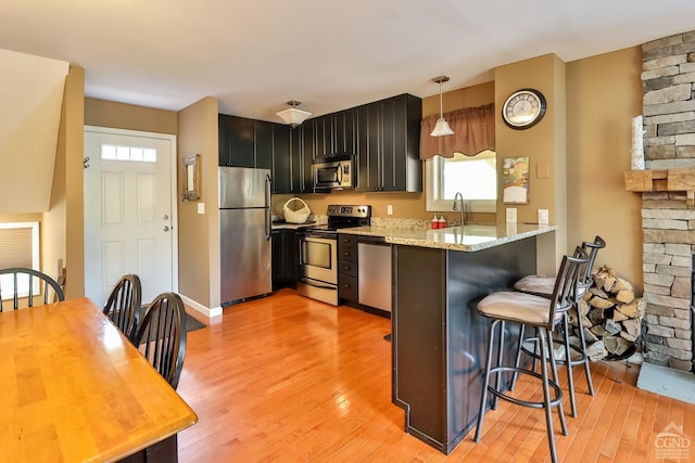 kitchen with kitchen peninsula, a kitchen breakfast bar, stainless steel appliances, pendant lighting, and light hardwood / wood-style flooring