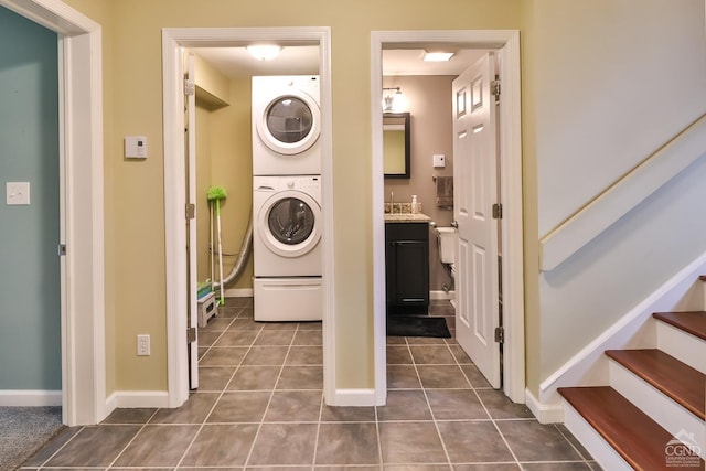 laundry area with dark tile patterned floors and stacked washer / drying machine