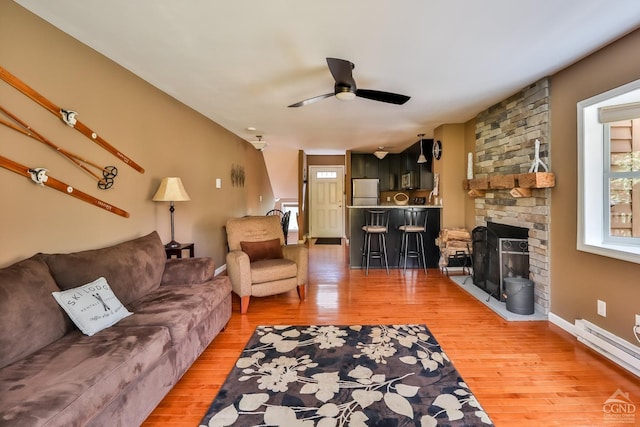 living room with ceiling fan, a fireplace, a baseboard radiator, and hardwood / wood-style flooring