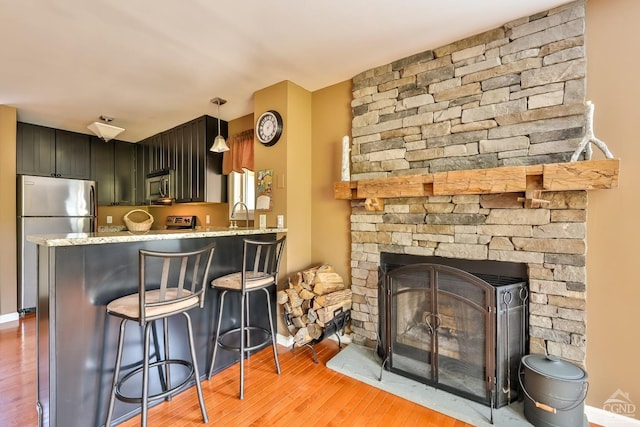 kitchen featuring a kitchen breakfast bar, kitchen peninsula, a fireplace, appliances with stainless steel finishes, and light wood-type flooring