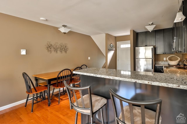 kitchen with a kitchen breakfast bar, light stone countertops, light hardwood / wood-style floors, and appliances with stainless steel finishes