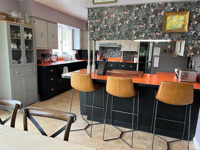 kitchen featuring a sink, under cabinet range hood, glass insert cabinets, a kitchen breakfast bar, and appliances with stainless steel finishes