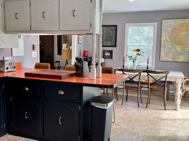 kitchen featuring a toaster, light countertops, dark cabinetry, white cabinetry, and a peninsula