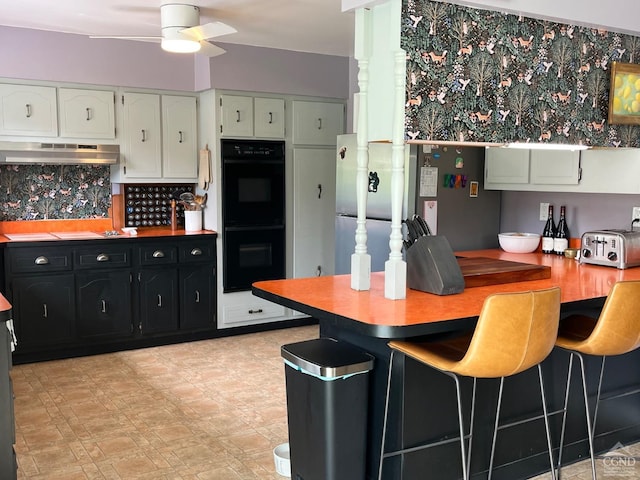 kitchen featuring under cabinet range hood, a ceiling fan, white cabinetry, dobule oven black, and dark cabinets
