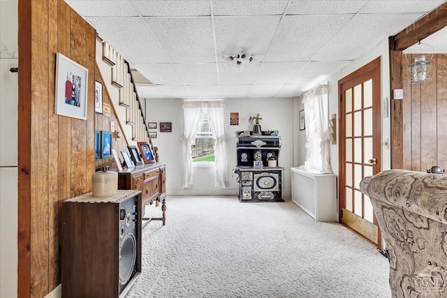 interior space with wooden walls, carpet floors, stairway, and a drop ceiling