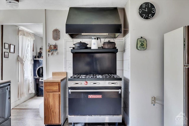 kitchen featuring stainless steel range with gas stovetop, light countertops, brown cabinetry, wall chimney exhaust hood, and freestanding refrigerator