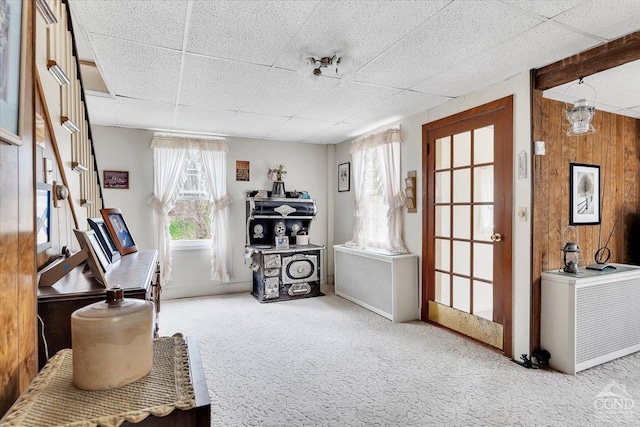 living area featuring carpet flooring, wooden walls, and a paneled ceiling