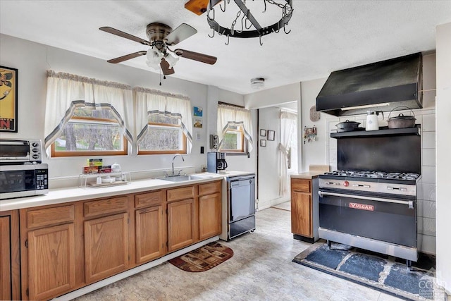 kitchen featuring brown cabinetry, appliances with stainless steel finishes, a sink, light countertops, and wall chimney exhaust hood