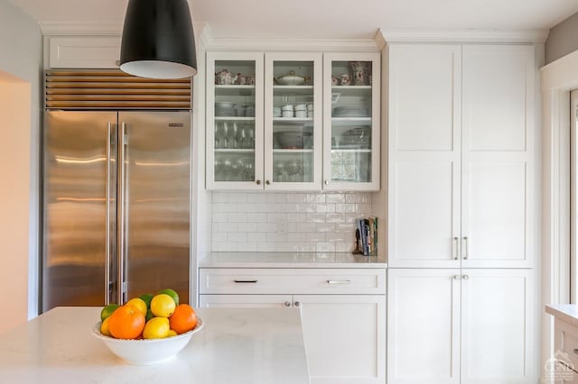 kitchen featuring light stone countertops, decorative backsplash, white cabinets, and built in fridge