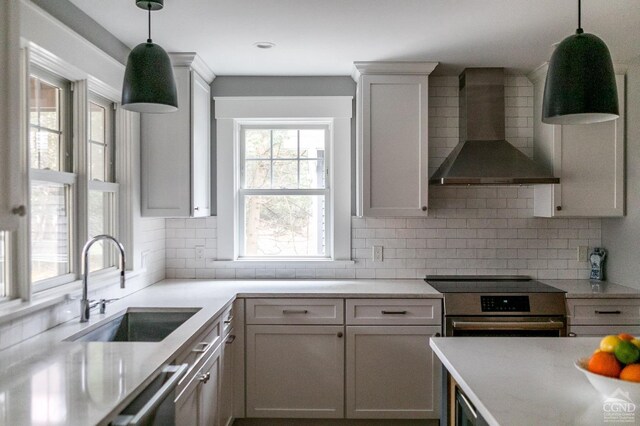 kitchen featuring backsplash, sink, wall chimney range hood, and hanging light fixtures