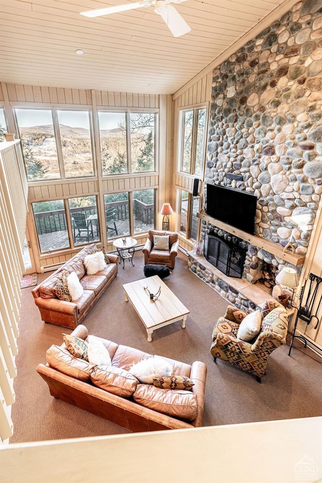 living room featuring wood ceiling, ceiling fan, a stone fireplace, and carpet floors