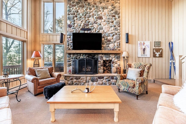 carpeted living room with a baseboard heating unit, a stone fireplace, wooden walls, and a towering ceiling