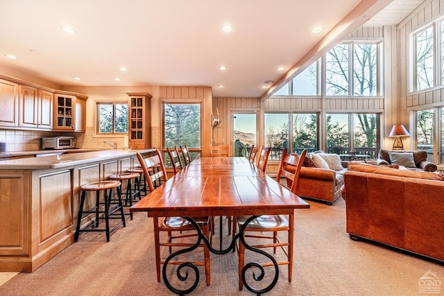 dining space featuring a high ceiling, light colored carpet, and wooden walls