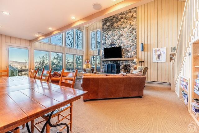 living room featuring baseboard heating, a towering ceiling, wooden walls, carpet flooring, and a fireplace