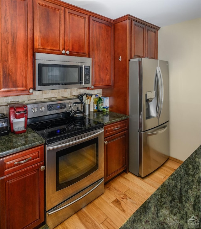 kitchen featuring appliances with stainless steel finishes, light wood-type flooring, decorative backsplash, and dark stone countertops