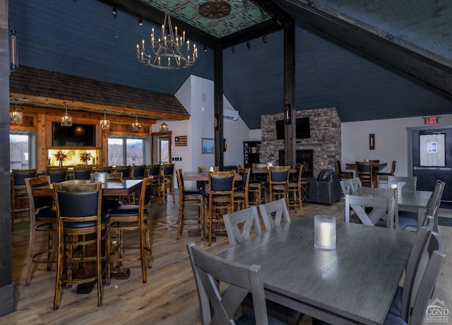 dining room with a notable chandelier, hardwood / wood-style floors, a stone fireplace, and high vaulted ceiling