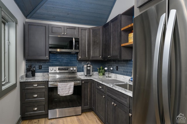 kitchen with dark brown cabinetry, vaulted ceiling, light wood-type flooring, stainless steel appliances, and decorative backsplash