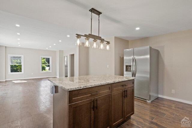 kitchen featuring stainless steel fridge, light stone counters, dark wood-type flooring, a center island, and hanging light fixtures