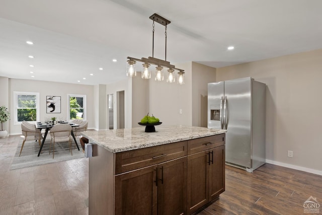 kitchen featuring a center island, dark wood-type flooring, hanging light fixtures, light stone countertops, and stainless steel fridge with ice dispenser