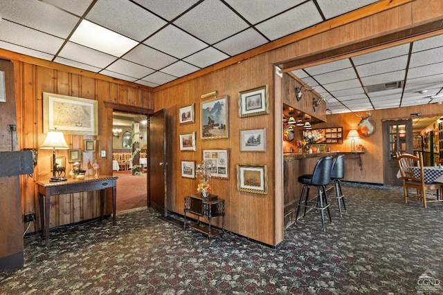 bar featuring a paneled ceiling, wood walls, and dark colored carpet