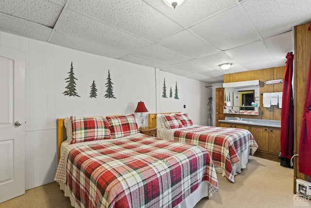 carpeted bedroom featuring a paneled ceiling and wooden walls