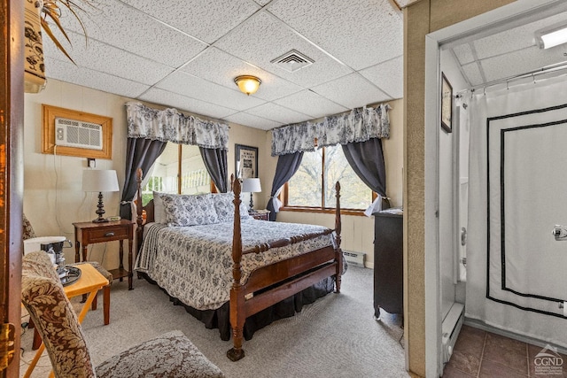 bedroom with a wall unit AC, a drop ceiling, carpet floors, and baseboard heating