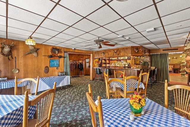 dining room featuring bar area, ceiling fan, carpet, and wood walls