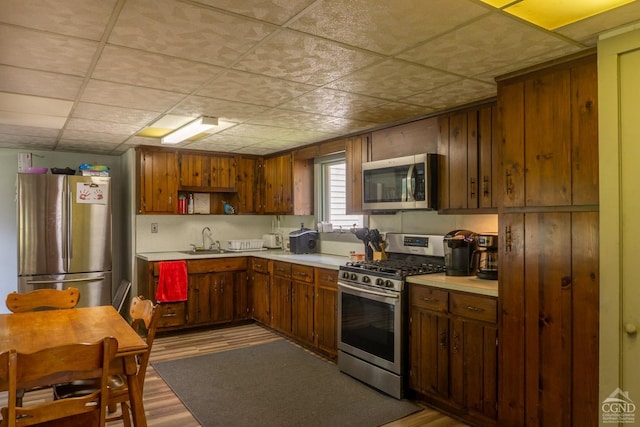 kitchen featuring a paneled ceiling, light wood-type flooring, sink, and appliances with stainless steel finishes