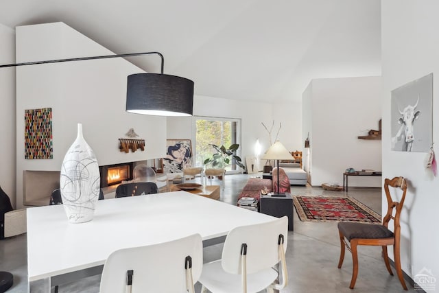 dining space with a warm lit fireplace, high vaulted ceiling, and finished concrete floors