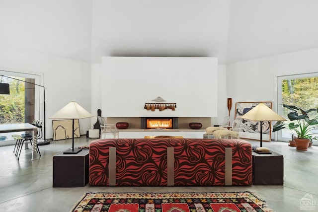 living area with a lit fireplace, finished concrete flooring, and a towering ceiling