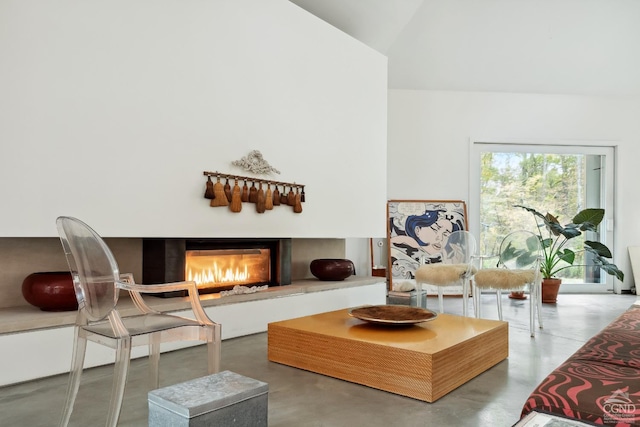 living area featuring concrete floors, lofted ceiling, and a glass covered fireplace
