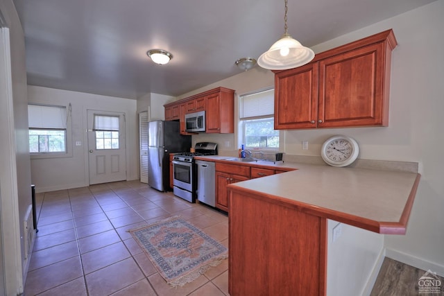 kitchen featuring kitchen peninsula, appliances with stainless steel finishes, light tile patterned floors, and pendant lighting