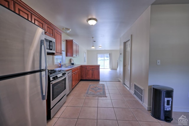 kitchen featuring kitchen peninsula, appliances with stainless steel finishes, decorative light fixtures, and light tile patterned floors