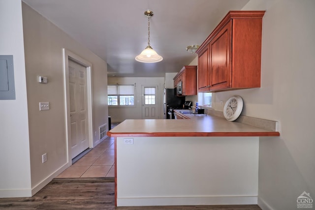 kitchen featuring kitchen peninsula, light wood-type flooring, stainless steel appliances, decorative light fixtures, and electric panel