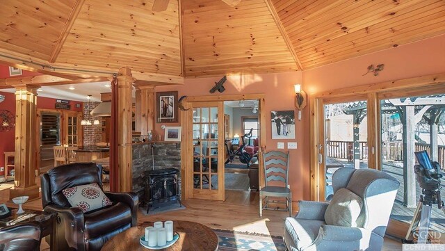 living room featuring decorative columns, wood ceiling, high vaulted ceiling, light hardwood / wood-style flooring, and a wood stove