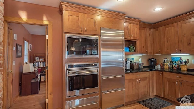 kitchen with built in appliances, dark stone countertops, and light hardwood / wood-style flooring