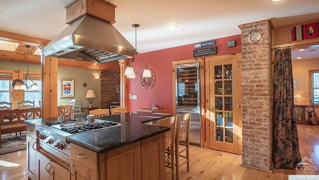 kitchen with stainless steel gas stovetop, a center island, hanging light fixtures, light hardwood / wood-style floors, and island range hood