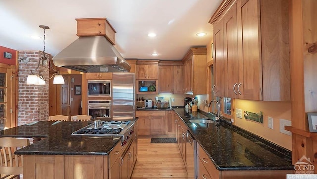 kitchen with island range hood, sink, built in appliances, light hardwood / wood-style flooring, and dark stone countertops