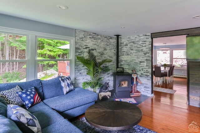 living room featuring wood-type flooring, a wood stove, baseboard heating, and a wealth of natural light