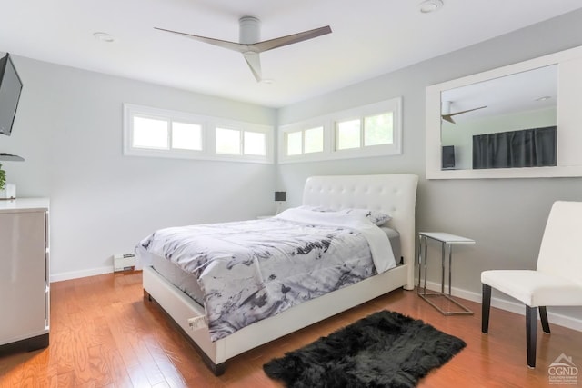 bedroom featuring hardwood / wood-style floors, baseboard heating, multiple windows, and ceiling fan