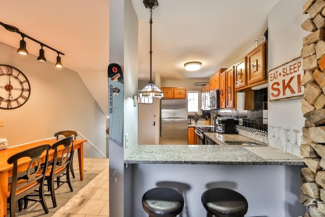 kitchen with a kitchen bar, light stone counters, hanging light fixtures, appliances with stainless steel finishes, and kitchen peninsula