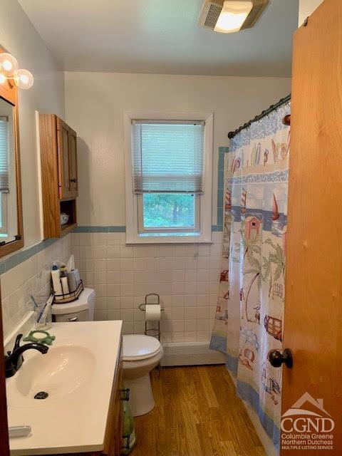 bathroom with curtained shower, wood-type flooring, toilet, vanity, and tile walls