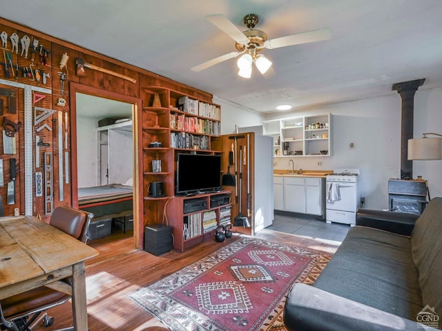 living room with wood walls, a wood stove, sink, ceiling fan, and light wood-type flooring