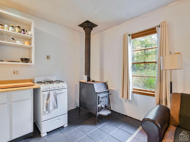 kitchen featuring white range with gas cooktop, white cabinets, dark tile patterned flooring, and a wood stove